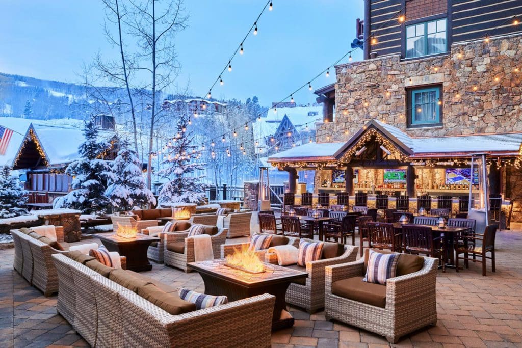 The outdoor terrace at The Ritz-Carlton, Bachelor Gulch, featuring soft outdoor lighting, fire pits, comfy chairs, and a view of the mountains in the distance.