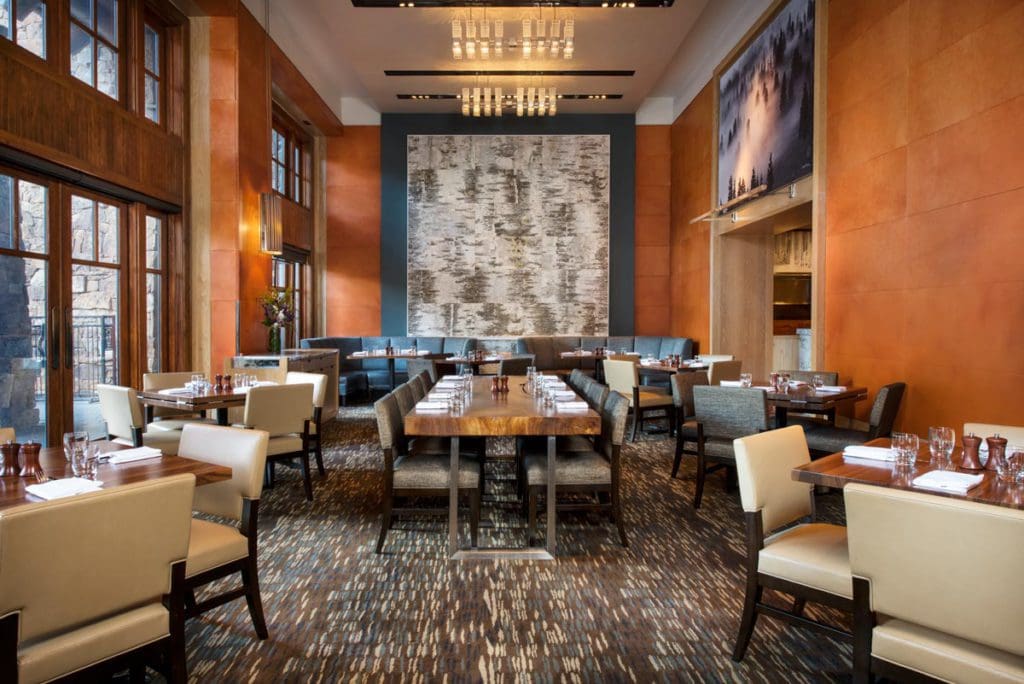 Inside one of the dining rooms at The Ritz-Carlton, Bachelor Gulch, featuring high-back chairs, warm furnishings, and wood accents.