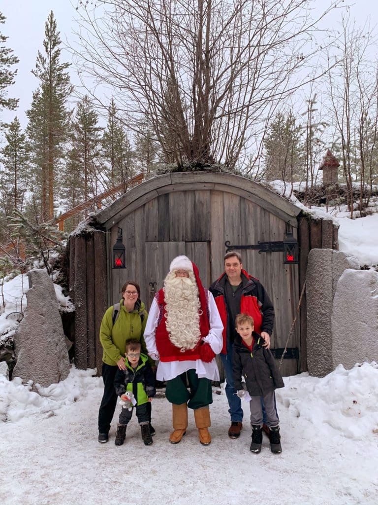 Two parents and their two kids stand near Santa in Lapland.