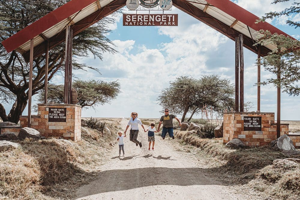 A family of four jumps together under the entrance sign to the Serengeti Park.