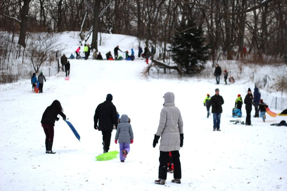 Several people enjoy fresh snow and a day of sledding at Central Park in NYC, one of the best places for a White Christmas in the United States for families.