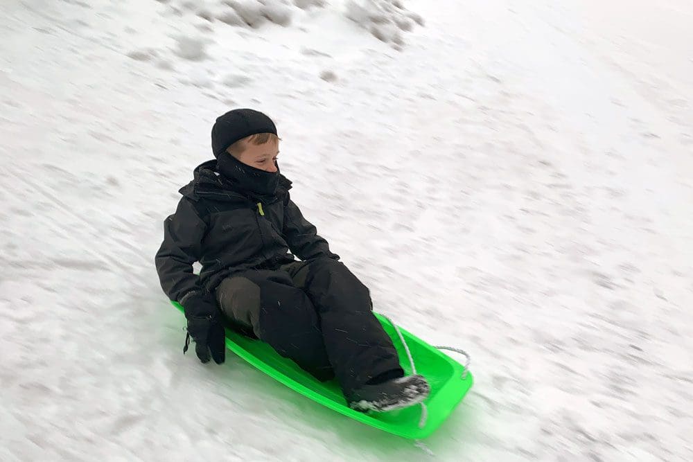 A young boy on a green sled soars down a snowy sledding hill in Washington DC.