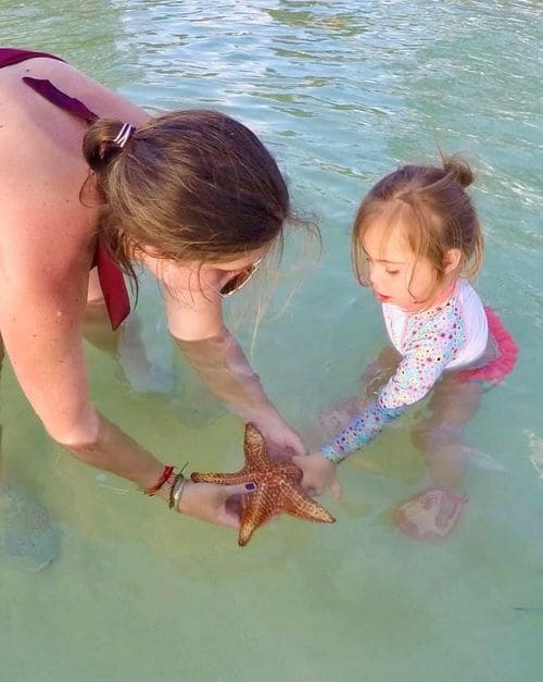 A mom and young daughter hold a starfish in the water, while visiting the Cayman Islands.