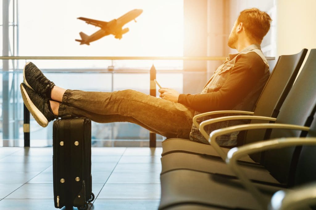 A man since at the airport looking out the window onto an aircraft taking off.