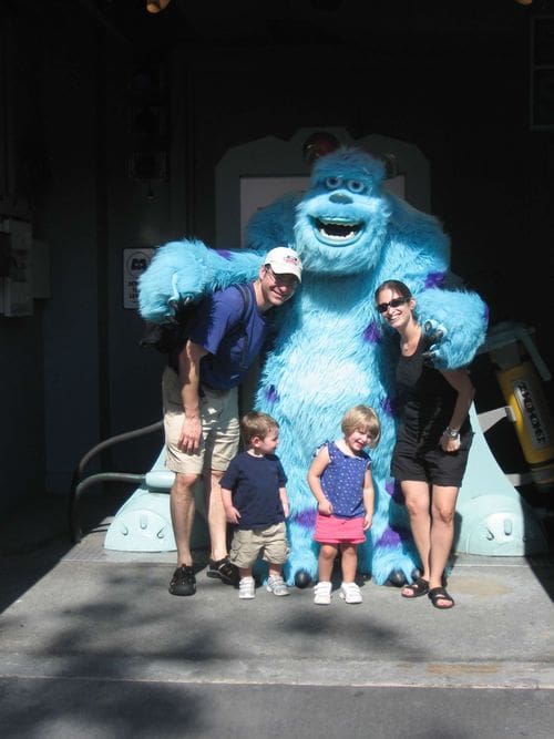 Two parents and their two young kids stand with Sully from Monsters Inc. while visiting the Disney parks.
