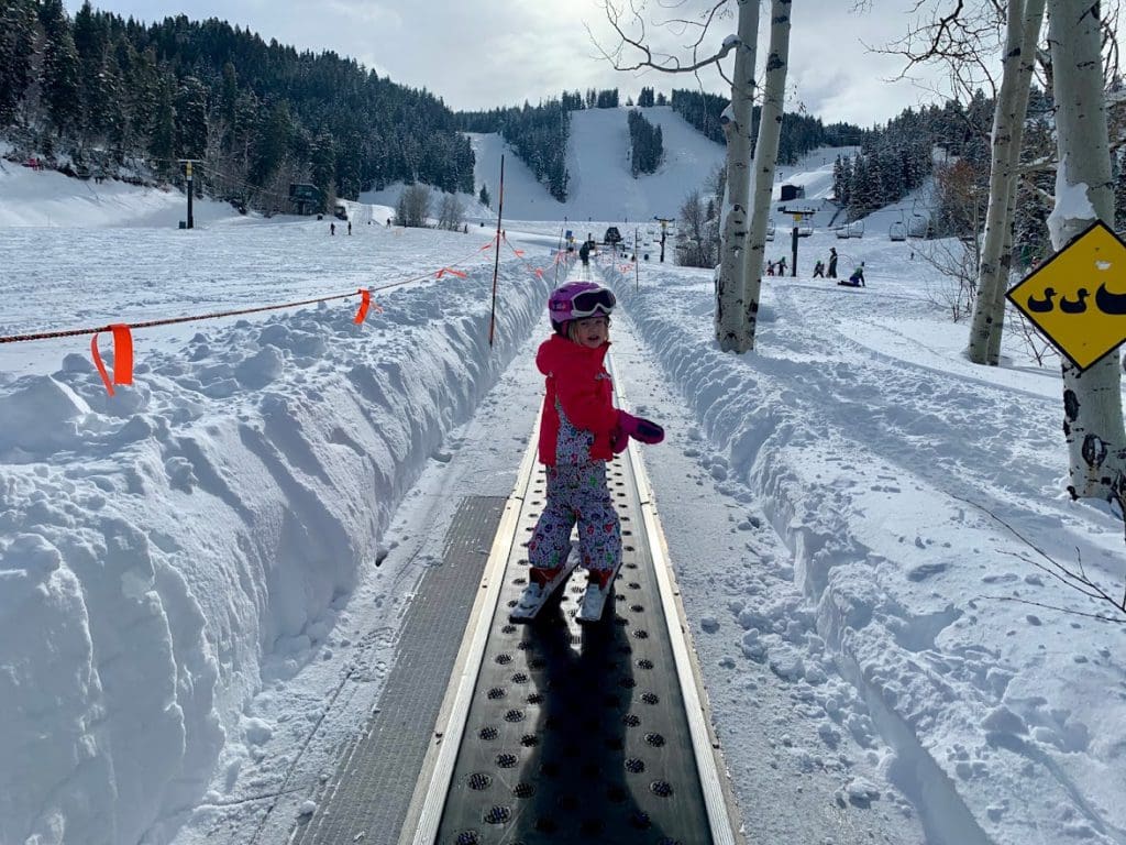 A young girl rides the magic carpet up the ski run in Park City, one of the best ski resorts in Utah for families.