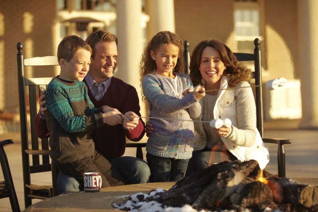 A family of four roast marshmallows over and outdoor fire at Hotel Hershey.