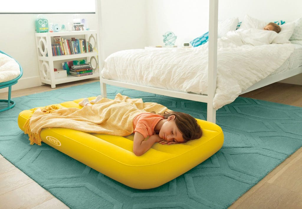 A young girl lays down on a yellow Intex Kids Travel Bed in her room.