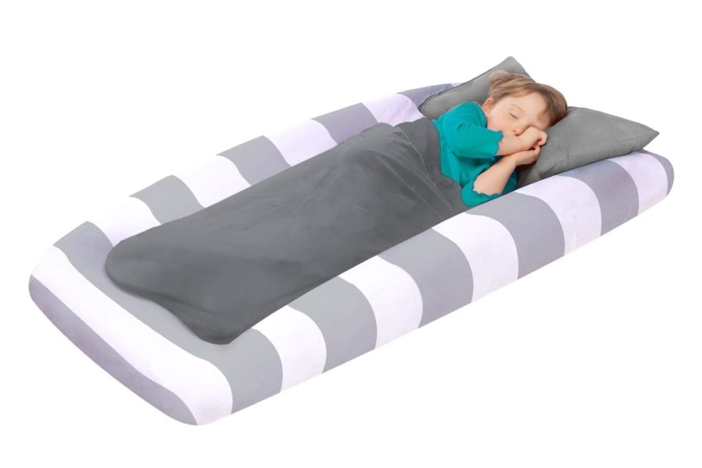 A young boy sleeps on a great and white The Shrunks Portable Toddler Travel Bed, with a gray blanket.