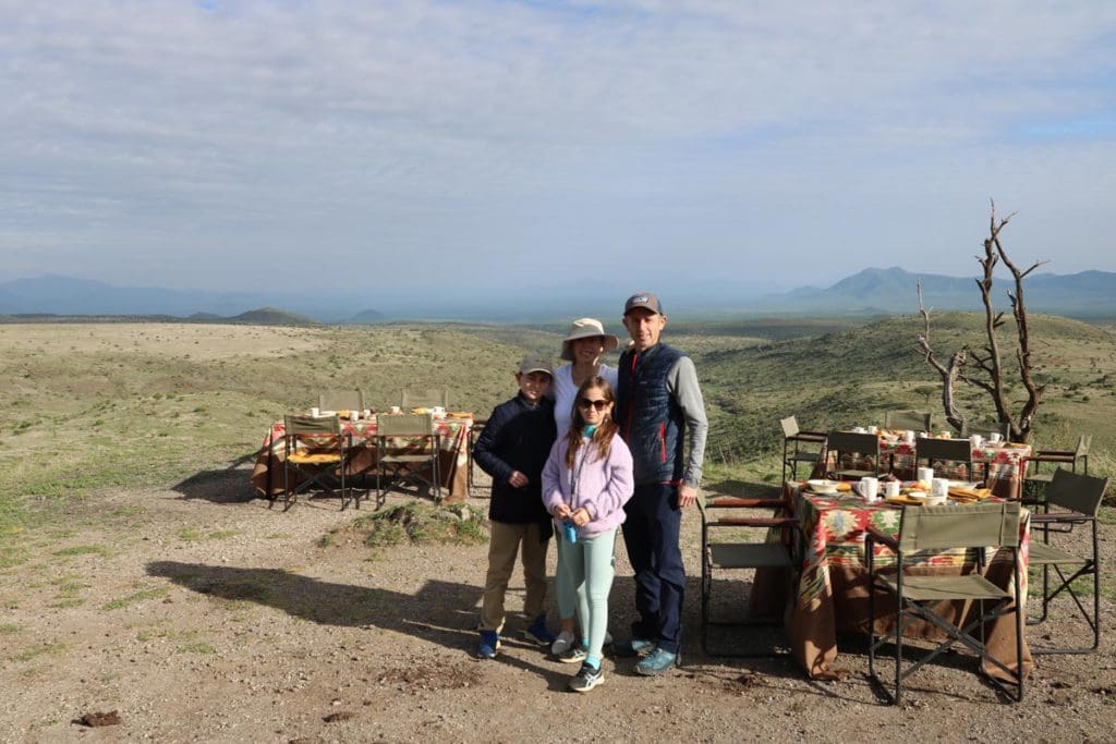 A family of four stands together near tables set for dinner, while on a safari in Kenya.