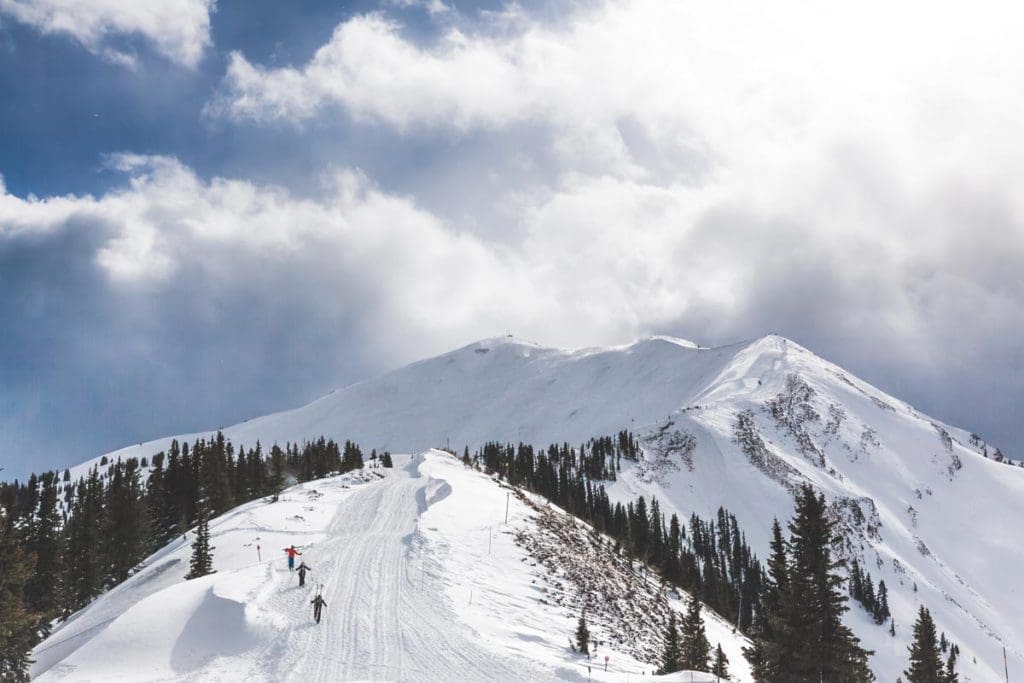 Three skiers fly down Aspen Highlands on skis on a sunny day.