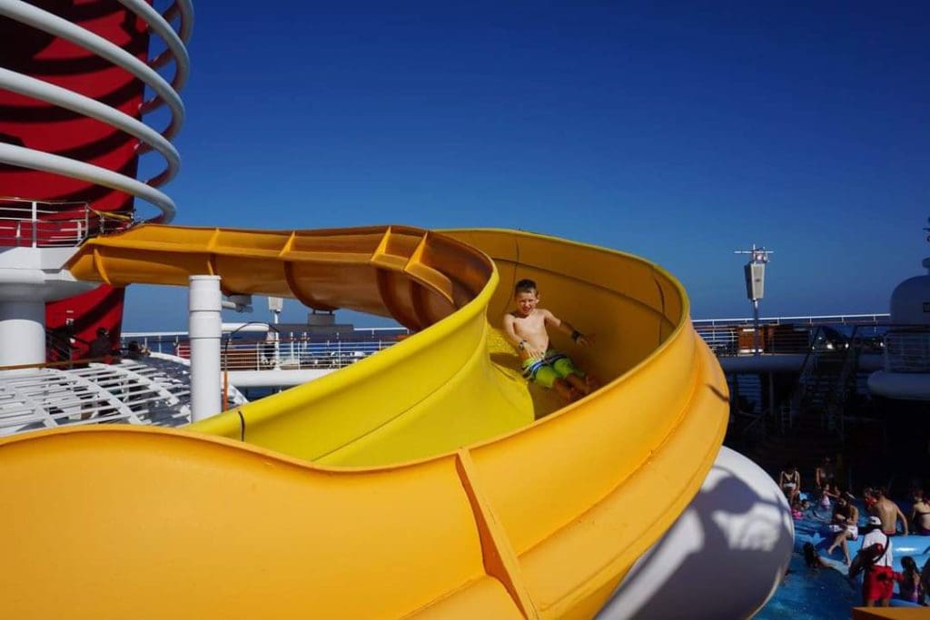 A young boy slides down a large yellow slide on a Disney Cruise ship.