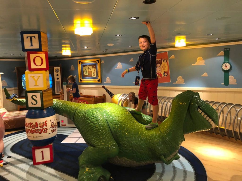 A young boy stands on a T-Rex inside the kids' club, while sailing with Disney Cruise Lines.