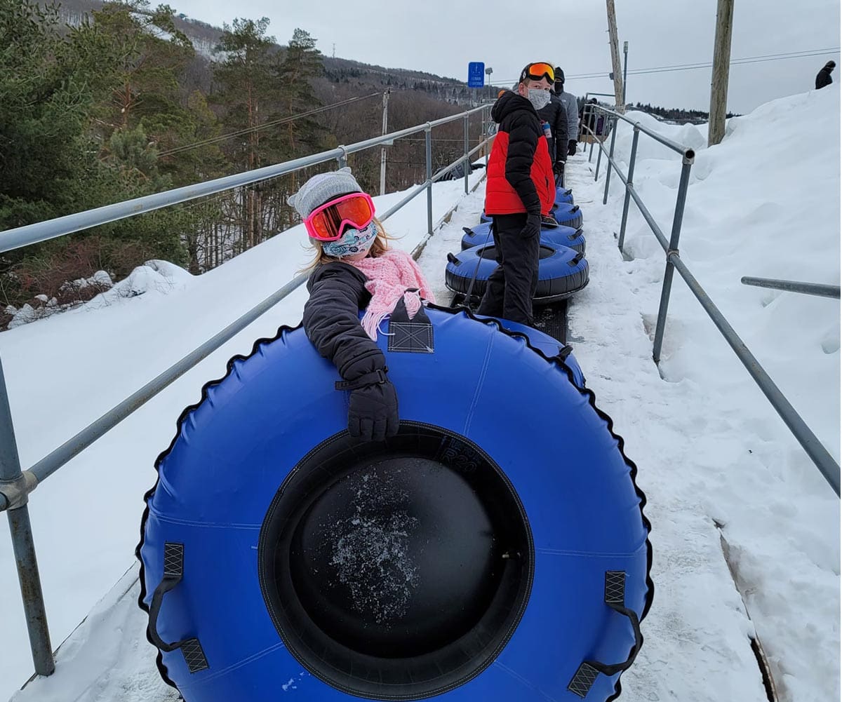 A young girl carries a blue snow tube up a hill to go snow tubing at Camelback Resort with her family.