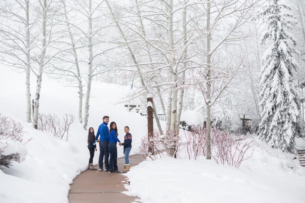 A family of four, all wearing blue, poses together on a beautiful winter day.