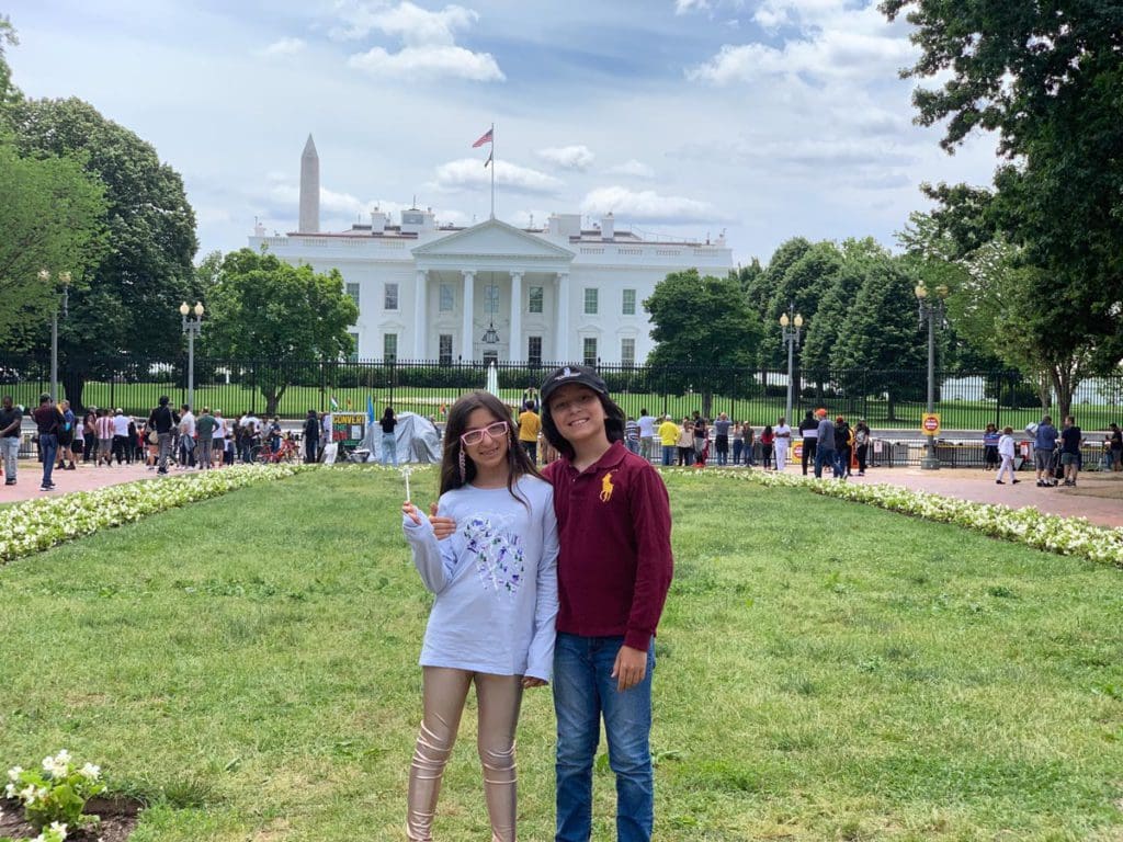 Two kids wave flags outside the White House lawn on a sunny day.