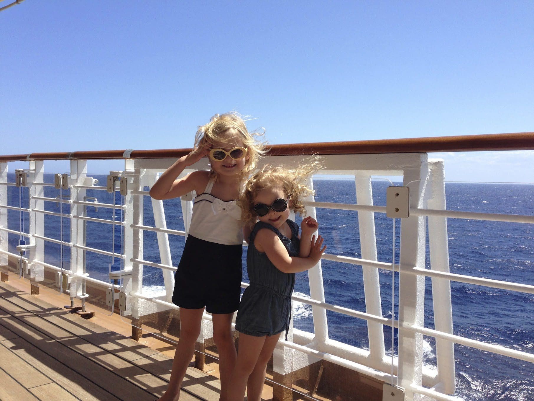 Two little girls stand on a deck aboard a Disney Cruise.