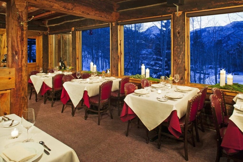 The interior dining room at Krabloonik, with white table cloths and red chairs, as well as a view of the mountains, one of the best places to eat when visiting Aspen during the winter with kids.
