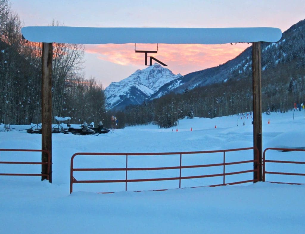 A view of Maroon Bell at dusk during the winter, with snowmobiles seen perched waiting for riders, one of the best things to do when visiting Aspen during the winter with kids.