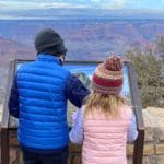 Two kids look at a plaque, while exploring the Grand Canyon as a family.