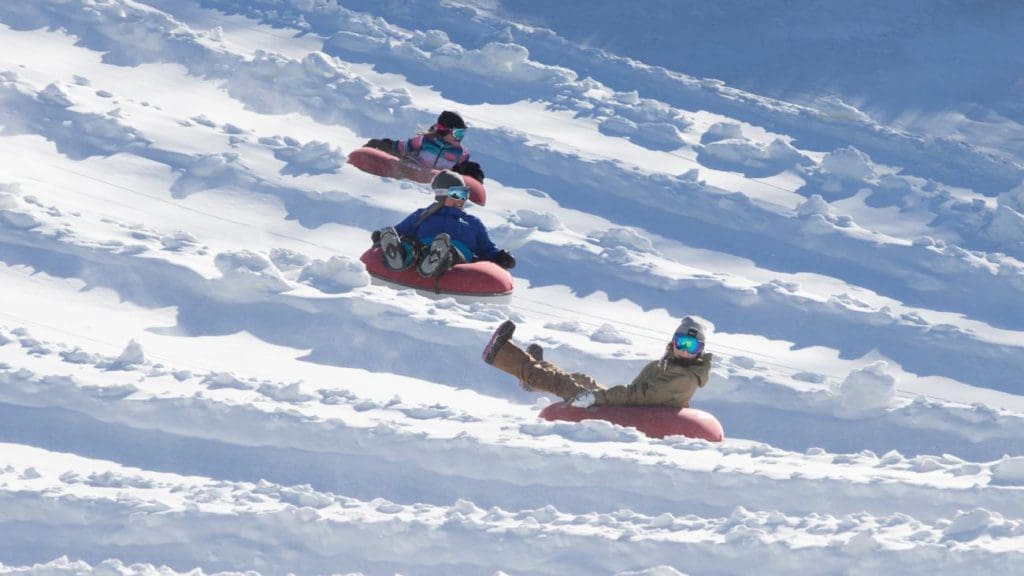 Three kids race down the hill on snow tubes at Bear Creek Resort.