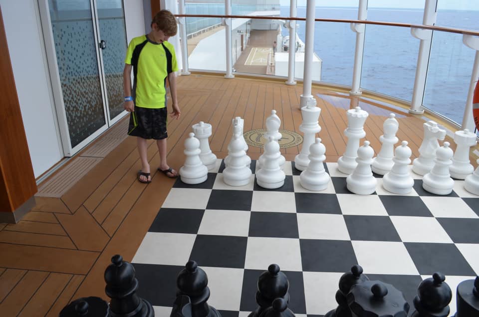 A young boy plays a large-scale game of chess on a Norwegian Cruise.
