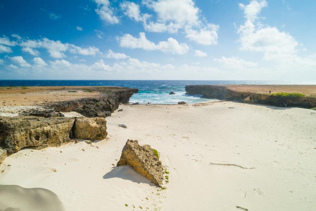 A view of Prins Beach, featuring rocks, sand, and the ocean beyond.