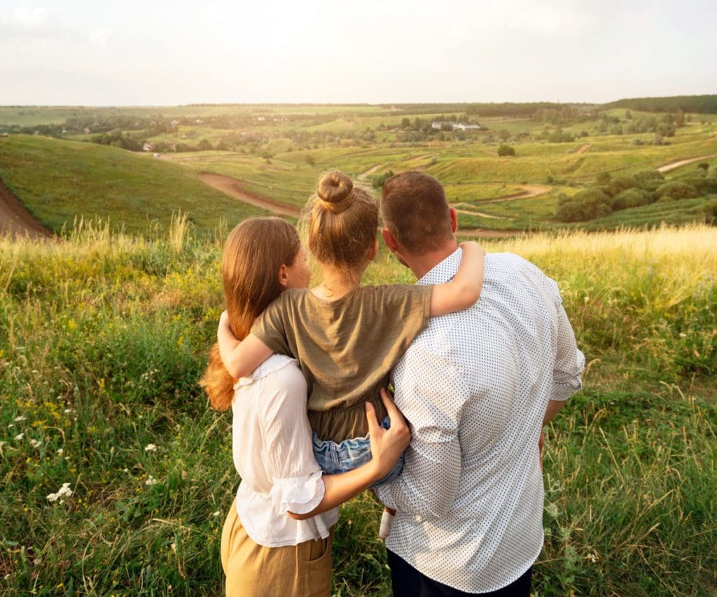 A family of three looks over a beautiful green, grassy scene together.