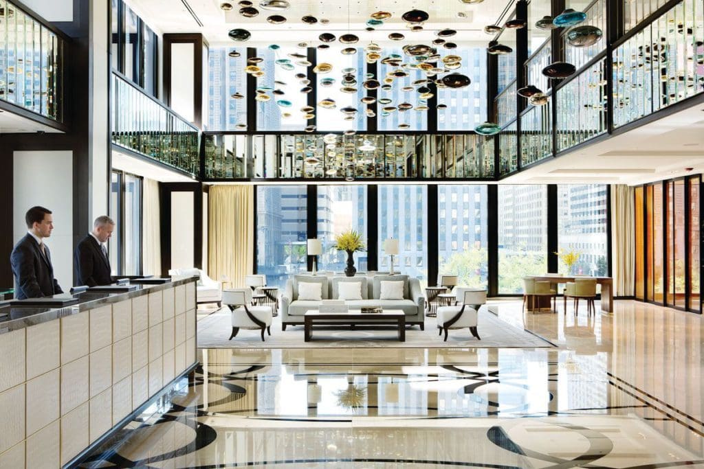 The stunning lobby of The Langham, Chicago, featuring floor to ceiling windows, luxe furnishings, and two staff members standing at the desk.