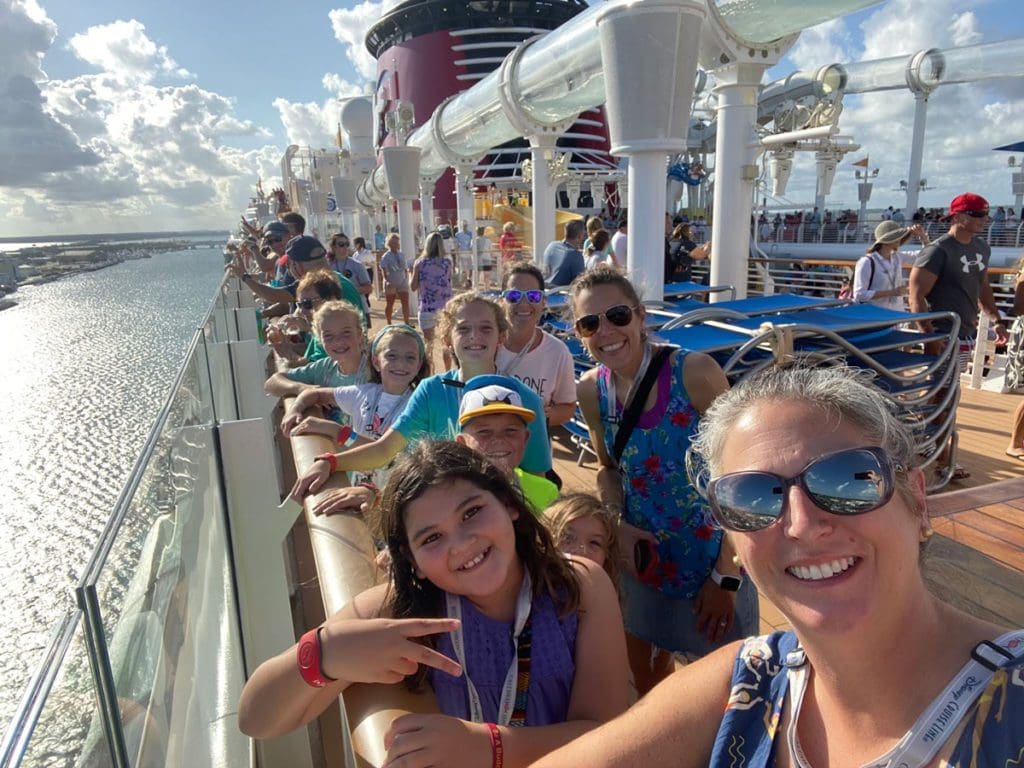 A large, multi-generational family lines up along the railing of a Disney Cruise ship to wave goodbye to port from one of the best cruise lines for families.