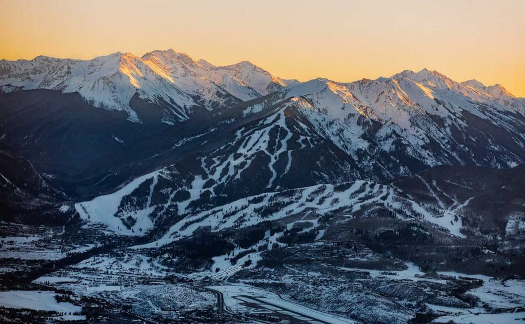 A view of Buttermilk Mountain at dusk, with a clear view of the snowy slopes between trees, one of the best mountains to ski when visiting Aspen during the winter with kids.
