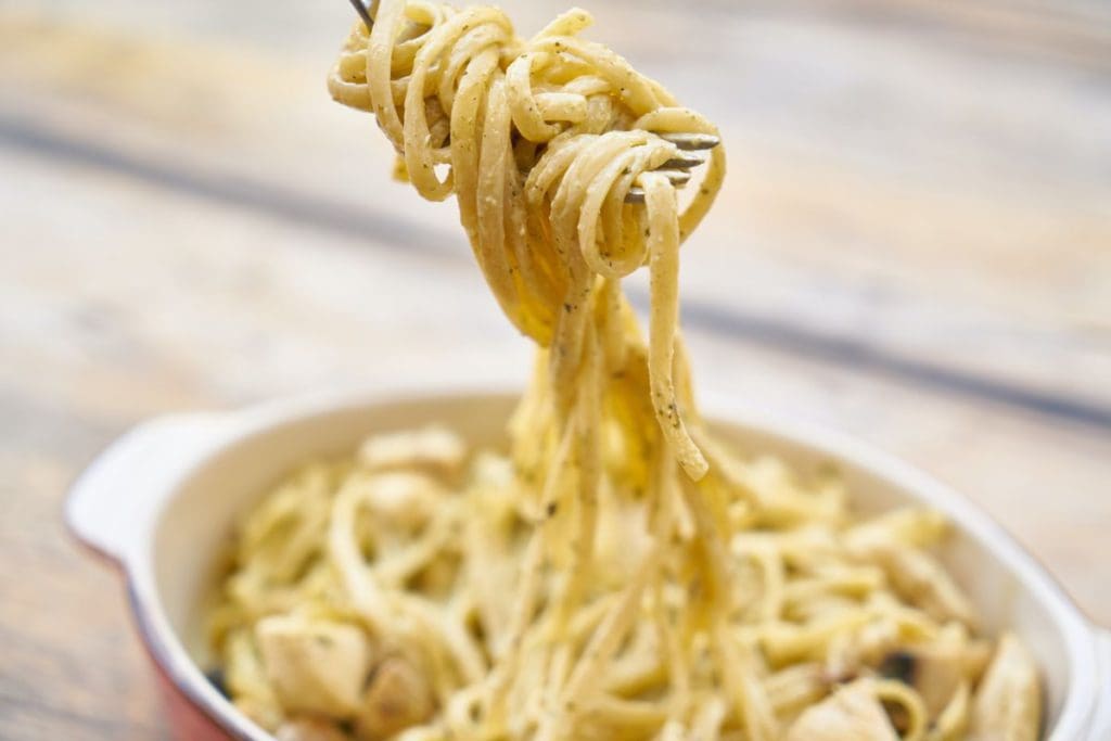 A fork lifts several noodles from a large dish of pasta.