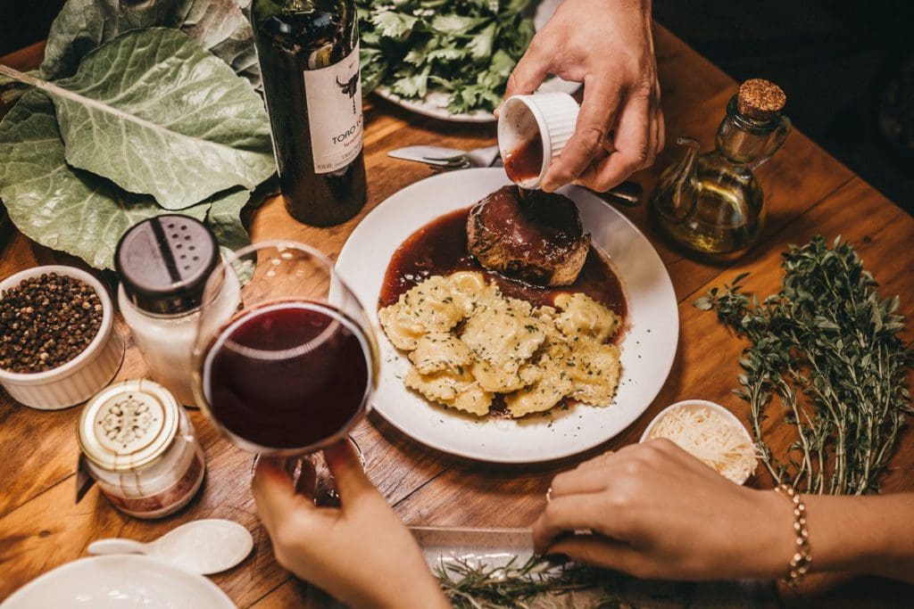 Two sets of hands prepare dinner on the table, featuring spices, ravioli, and other food, a lovely dinner is one of the best ways to add romance on a family road trip.