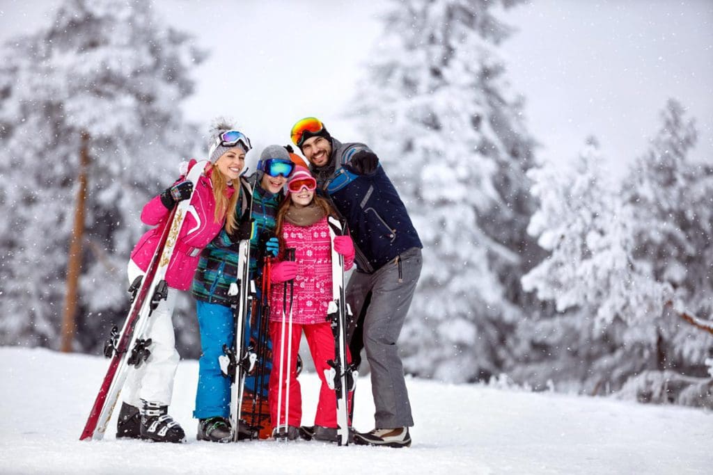 A family of four, all wearing colorful ski gear and skis, stands proudly on a winter landscape near Aspen.