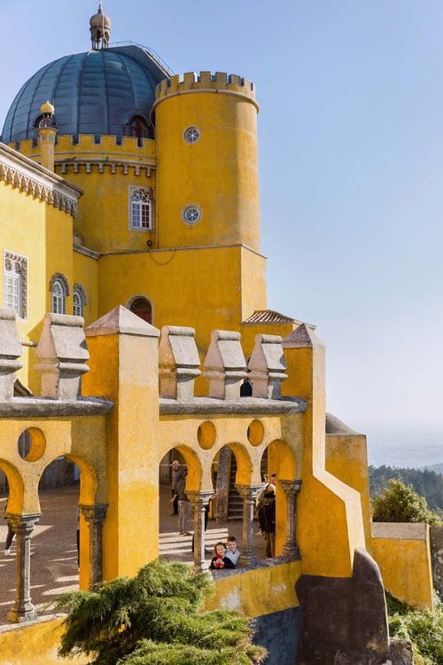 Kids sit along a ledge at a yellow castle in Sintra, near Lisbon.