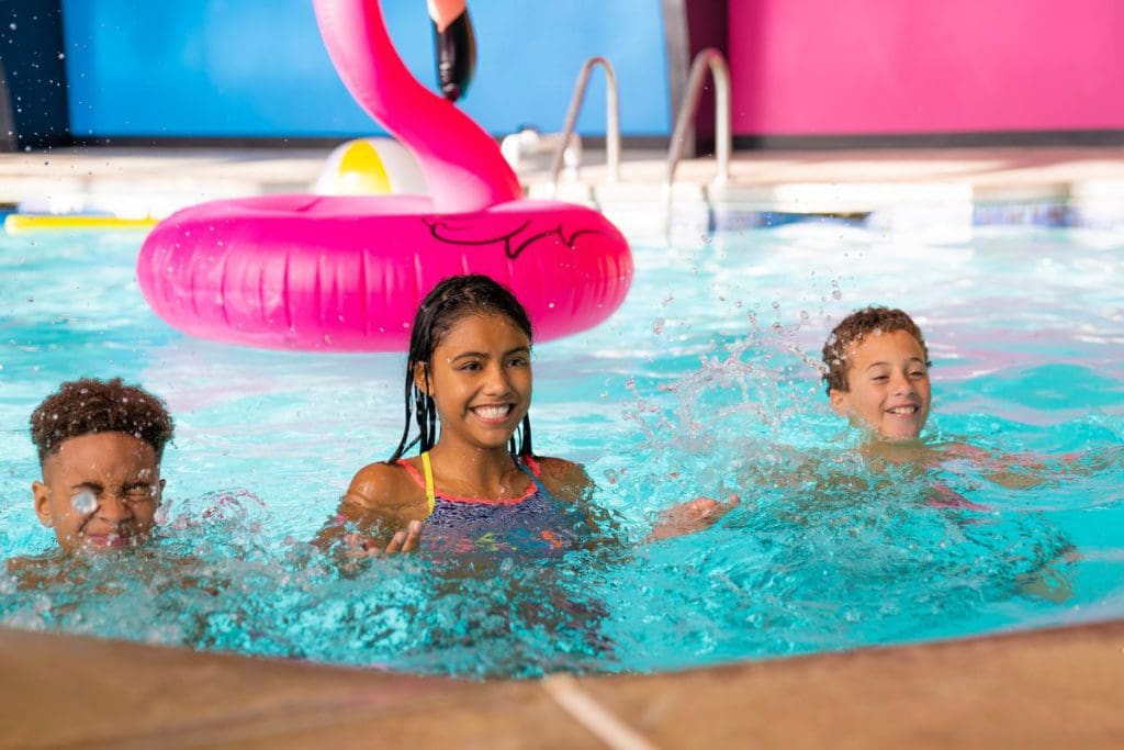 Three kids swim together in the hotel pool at the Cartoon Network Hotel, one of the best themed hotels in the United States for families.