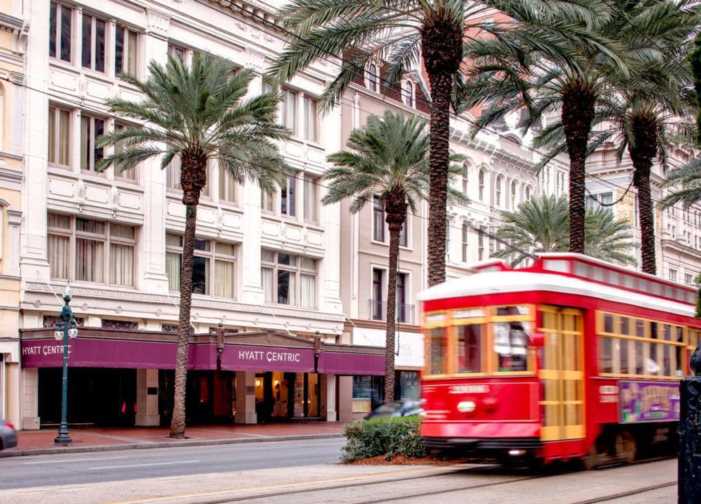 The exterior of Hyatt Centric French Quarter New Orleans, while a trolley passes by on a beautiful day at one of the best hotels in New Orleans for families.