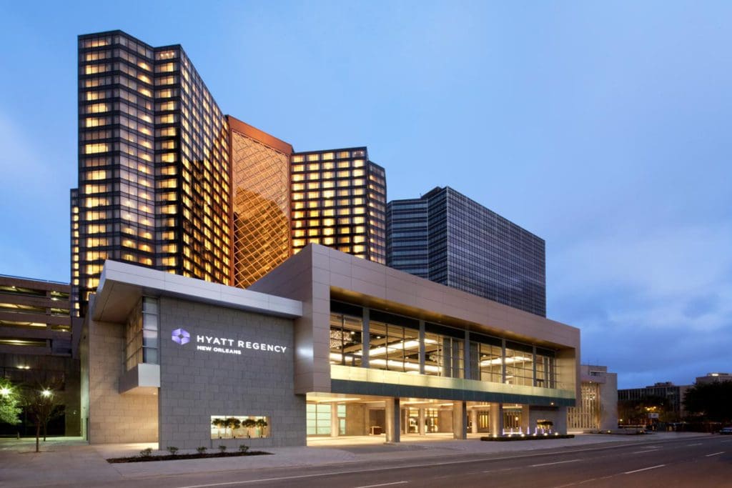 The exterior to the Hyatt Regency New Orleans, featuring a well-lit entrance and several stories of hotel rooms, all lit up at night.