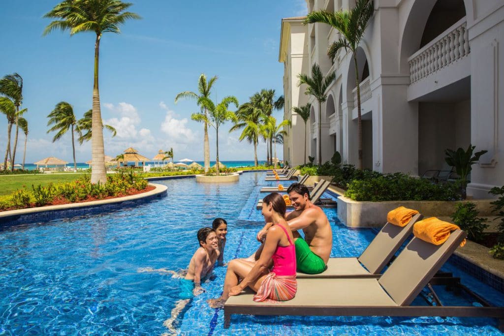 Parents sitting on poolside loungers talk to their kids who are swimming in the pool at the Hyatt Ziva Rose Hall.