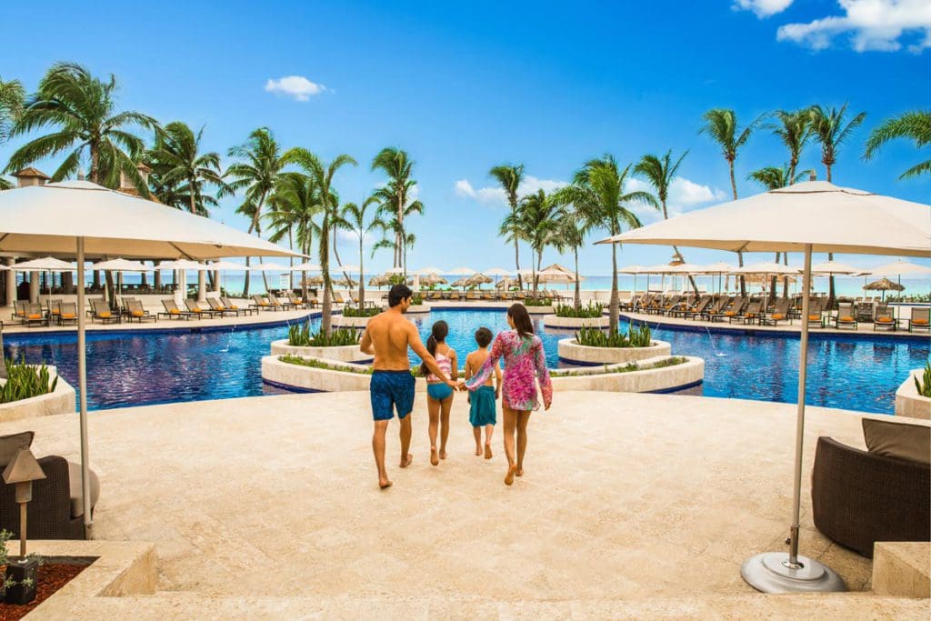 Two parents and their two children walk along the pool deck at the Hyatt Ziva Rose Hall, one of the best all-inclusive resorts in Jamaica for families.