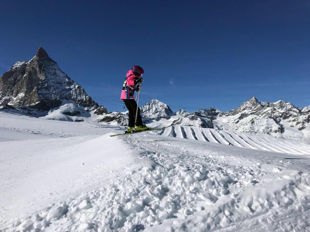 A young girl wearing a bright pink coat skis along a trail in Zermatt.