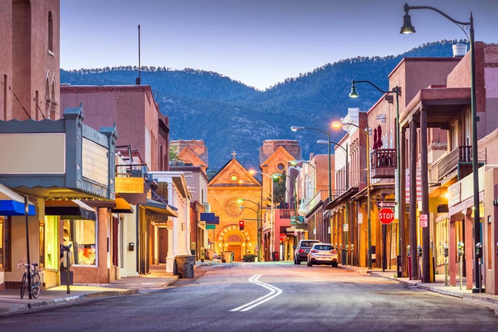 The main street in Santa Fe, one of the best American cities that feel like Europe for families, leading to a Spanish-style church, and mountains in the distance.