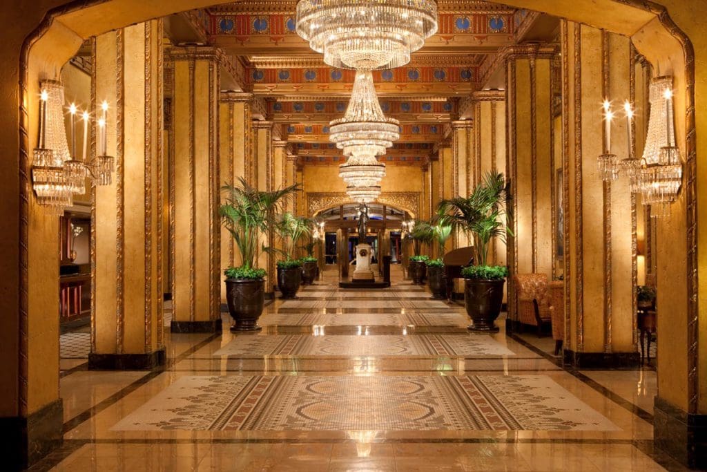 Inside the luxe lobby of The Roosevelt New Orleans, A Waldorf Astoria Hotel, featuring large chandeliers and opulent furnishings.