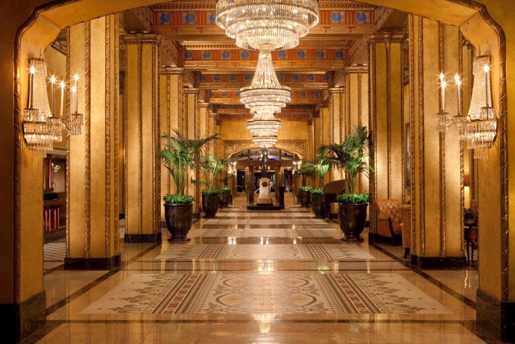 Inside the luxe lobby of The Roosevelt New Orleans, A Waldorf Astoria Hotel, featuring large chandeliers and opulent furnishings.