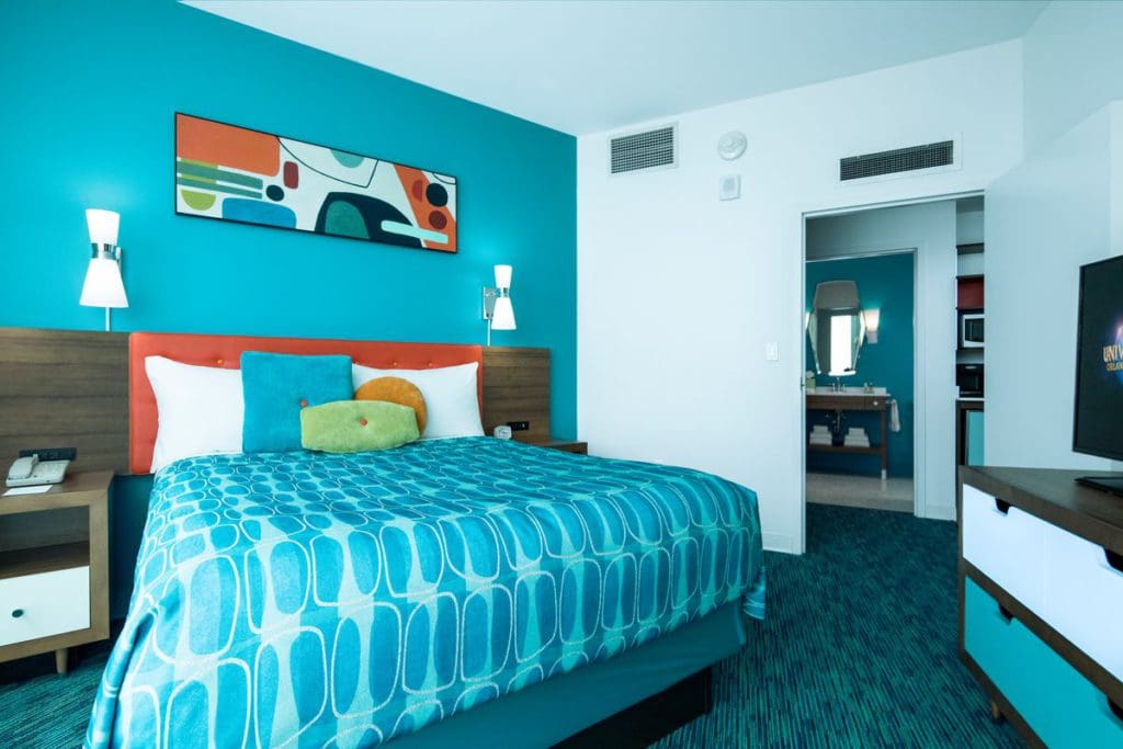 Inside a brightly colored room at Universal's Cabana Bay Beach Resort, featuring a large bed and furnishings in hues of blue, green, and orange.
