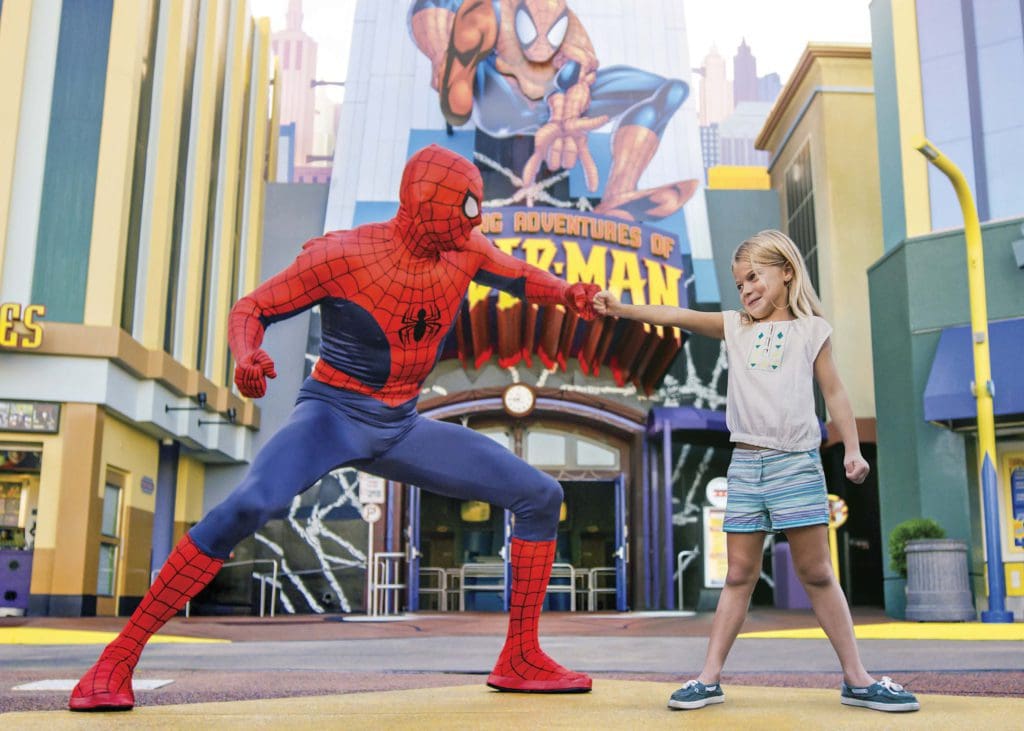 A young girl holds out a hand to Spiderman, who does the same at Universal Orlando, one of the best places for an East Coast road trip for families. 