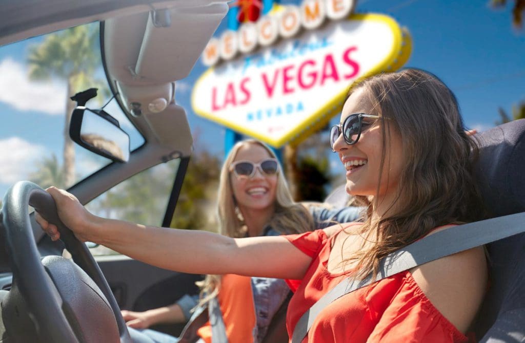 Two girls sitting in a convertible laugh, with the iconic Las Vegas sign behind them.