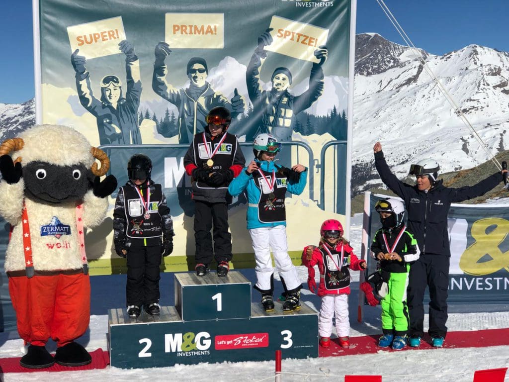 Kids stand at a medal podium after completing a week at a ski school in Zermatt.