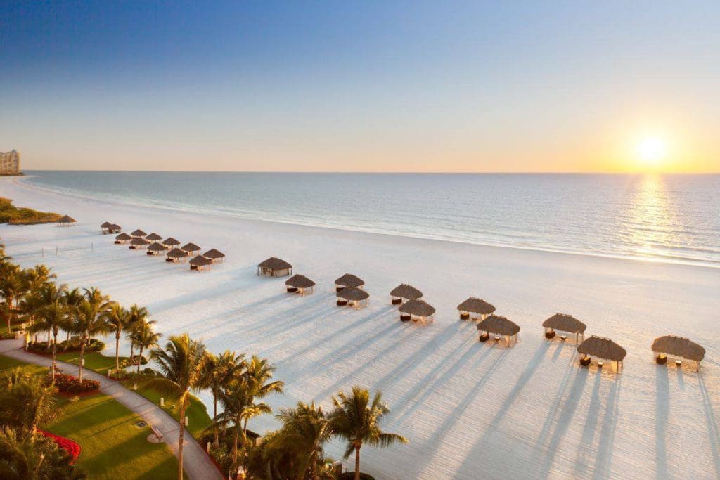An aerial view of the beach at JW Marriott Marco Island Resort, featuring a line of cabanas at sunset.