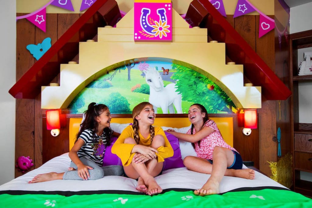 Three teen girls sit on a LEGO Friends-themed bed at LEGOLAND Hotel, one of the best themed hotels in the United States for families.